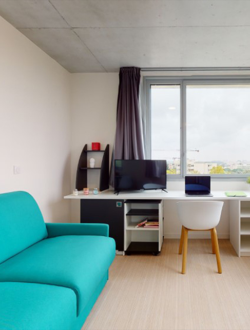 Studio étudiant avec un canapé turquoise, un bureau face à une fenêtre, une chaise design, une télévision et des rangements décorés.
