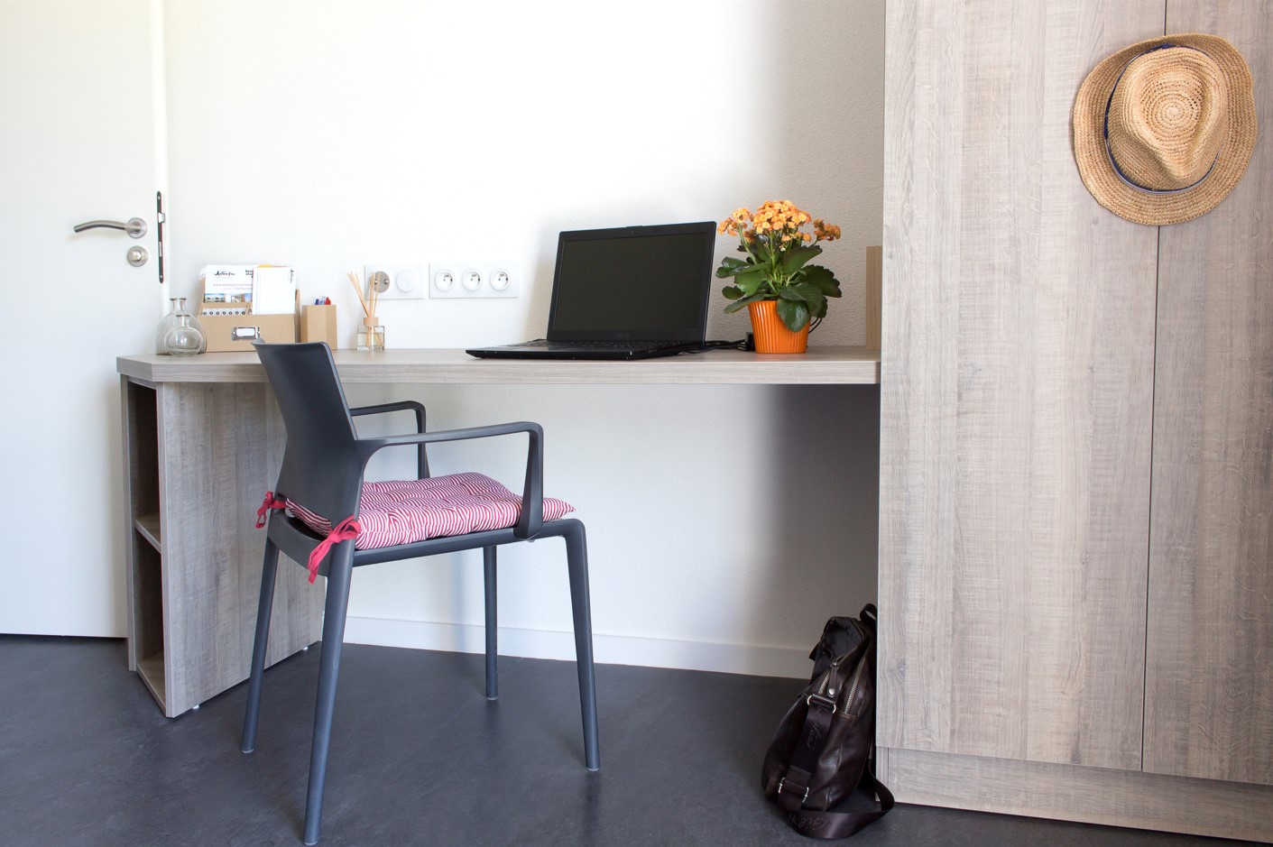 Bureau étudiant lumineux avec une chaise, un ordinateur portable fermé, une plante verte, des fournitures et une armoire en bois clair.