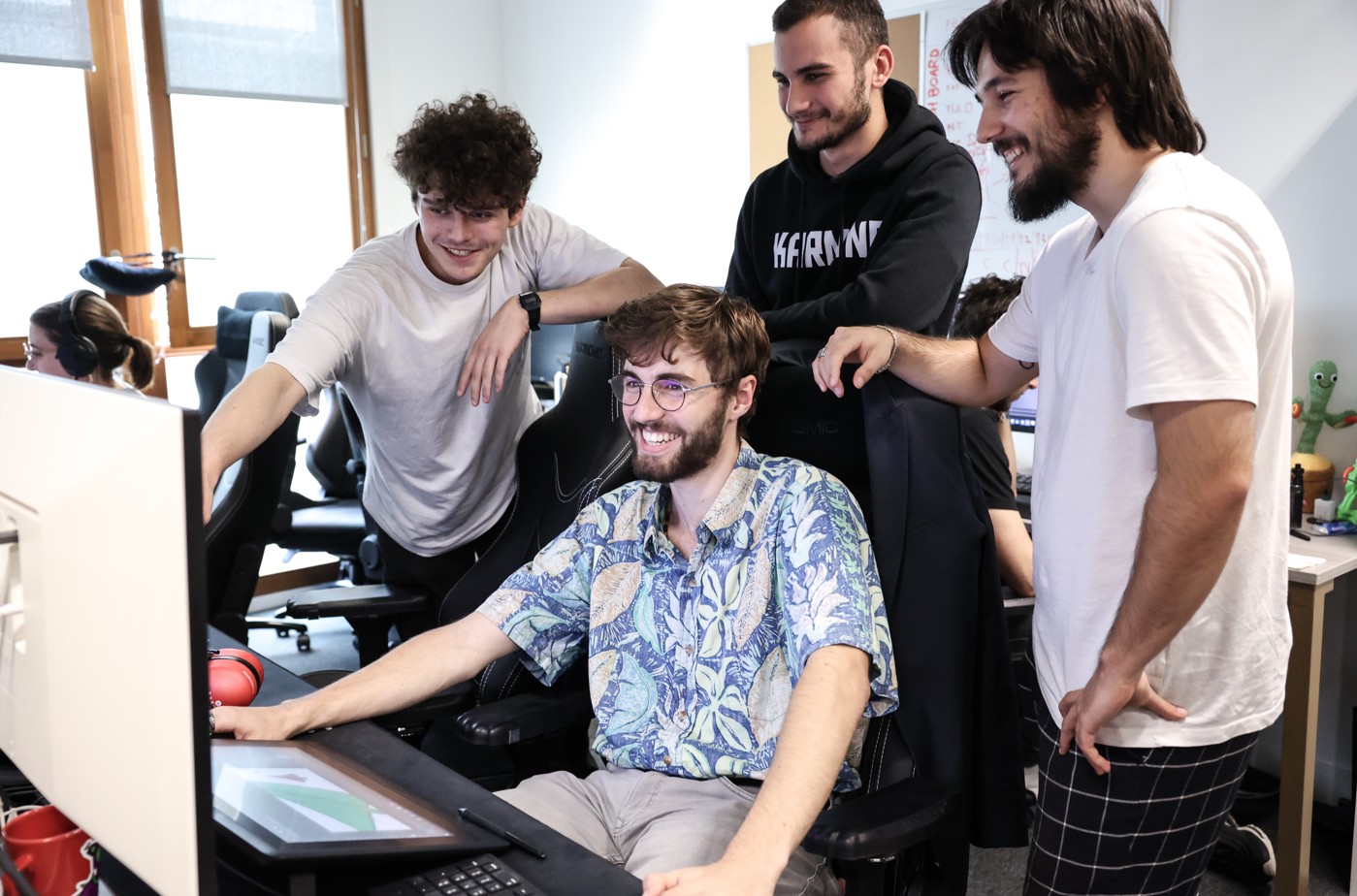 Quatre étudiants, souriants, collaborent autour d’un poste de travail informatique dans une salle équipée, concentrés sur un projet créatif.